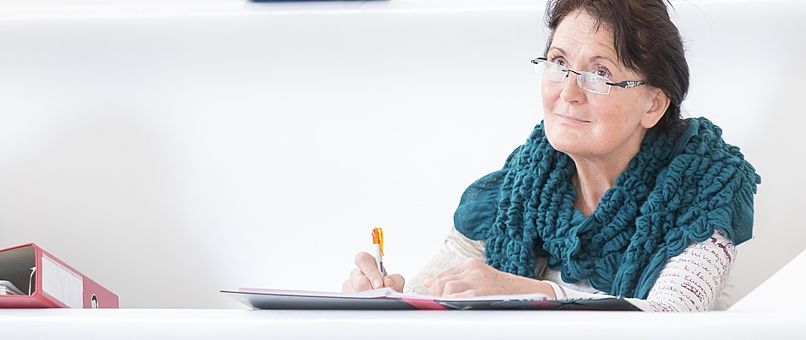 Eine ältere Dame mit Brille sitzt im Vorlesungssaal.